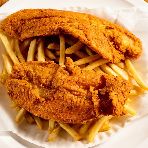 Two golden fried fish fillets and french fries on a white plate with tartar sauce and a fork.