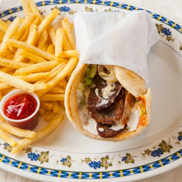 A gyro sandwich, french fries with ketchup, and a Pepsi on a patterned plate.