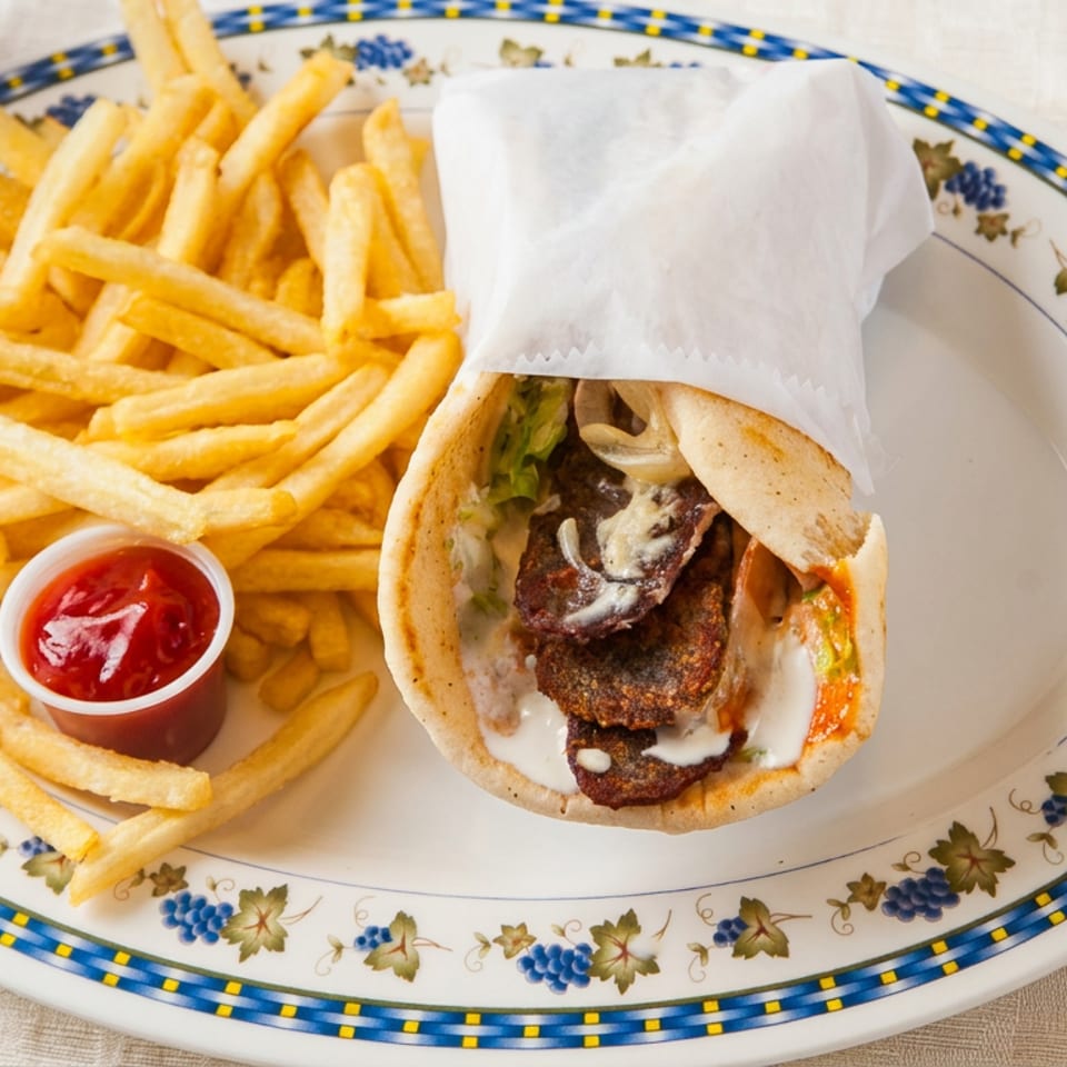 A gyro sandwich, french fries with ketchup, and a Pepsi on a patterned plate.